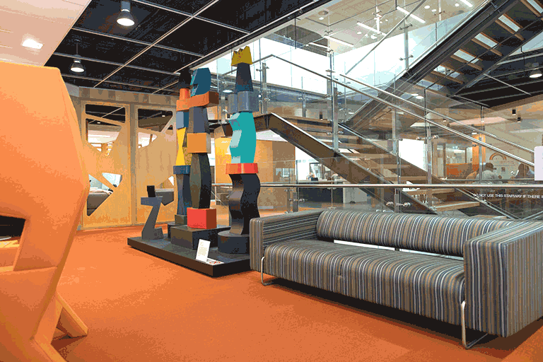 Office setting with orange carpet, grey couch and large multicoloured sculpture